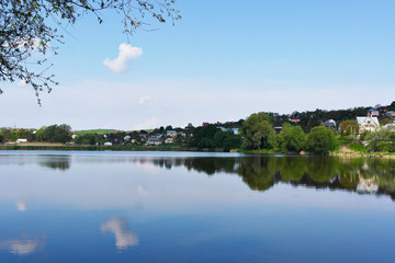 A lonely little cloud is reflected in a picturesque lake. Beautiful clean lake among the village.