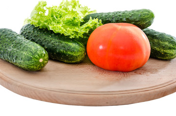 tomatoes, cucumbers and green salad on a wooden board on a white background