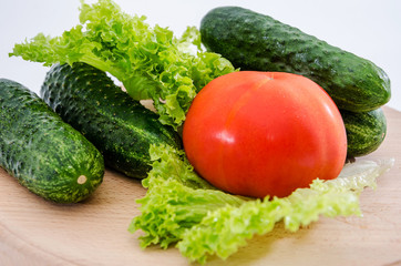 tomatoes, cucumbers and green salad on a wooden board on a white background