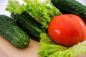 tomatoes, cucumbers and green salad on a wooden board on a white background