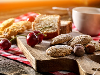 Oatmeal cookies and cherry on kitchen cutting board gingham checkered cotton fabric on table in village style for picnic with plate of macaron background. Sunshine on cupcake.