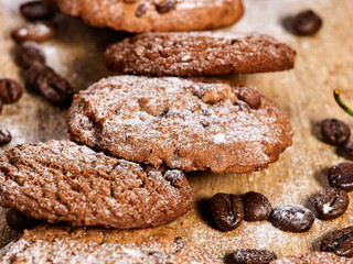 Oatmeal chocolate cookies with coffee grains and cherry, powdered sugar on kitchen cutting board with checkered fabric on wooden table in village style for picnic. Extremely beneficial products.