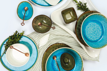 Fototapeta na wymiar Simple rustic handmade blue and green crockery against white wooden wall: dish, stack of bowls. Top view