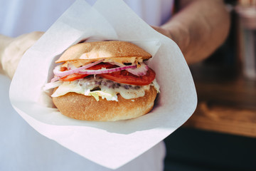 man holds burger with hands  on background in cafe