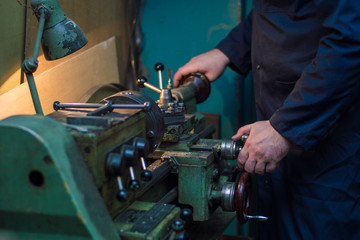 Professional worker in blue uniform operating industrial lathe grinding machine - metalworking industry concept. Closeup mechanical Engineering control lathe machine in factory workshop.