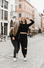 Happy friends having fun walking in city center. Beautiful young positive girls spend summer holidays. Two smiling pretty teenagers travel around old wonderful European city. Joint vacation concept