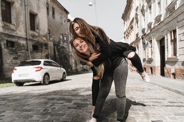 Fototapeta na wymiar Happy friends having fun walking in city center. Beautiful young positive girls spend summer holidays. Two smiling pretty teenagers travel around old wonderful European city. Joint vacation concept