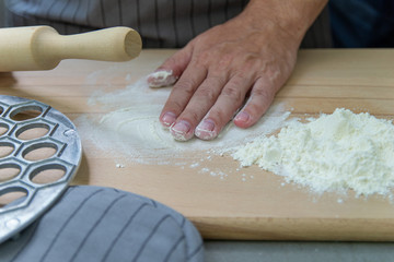 The hands of the chef knead the dough on a wooden table near the milling molds for ravioli rolling...