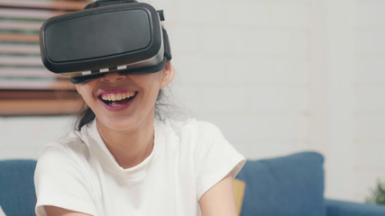 Asian teenager woman using glasses virtual reality simulator playing video games in living room, female feeling happy using relax time lying on sofa at home. Lifestyle women relax at home concept.