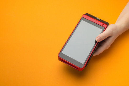 The cashier offers POS terminal for payment by credit card. Closeup, orange background, copy space. Concept for banking, shopping and contactless payments.