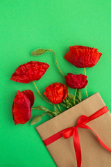 Red poppies in a envelope tied with a red  ribbon on the green  background.Top view.Copy space.Spring or summer flowers concept.