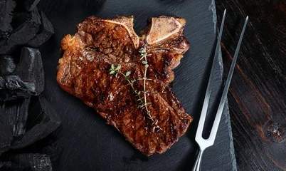 Fotobehang barbeque steak on a black slate board with meat fork and grill coals next to it © Mikhaylovskiy 