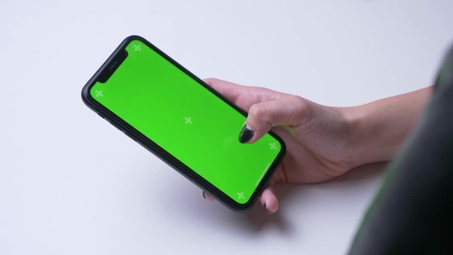 Closeup back view shoot of female hand messaging on the phone with green chroma screen in the office indoors on the white desk