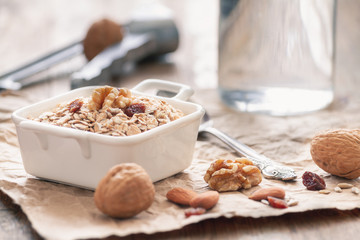 Oatmeal with walnuts, raisins and almonds in a white ceramic bowl on a vintage rustic wood background. Healthy nutrition breakfast concept.