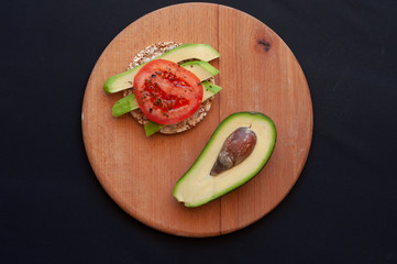 snack with avocado and tomato and half an avocado on wooden board