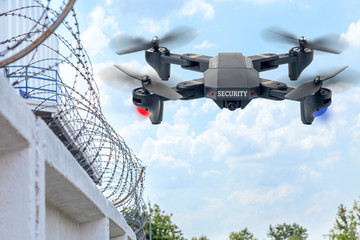 Security drone patrols the territory across the sky. Guarding the wall with barbed wire drone with blue and red beacon