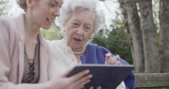 woman and senior grandmother using tablet device for video call at park.Granddaughter and grandma talking together with mobile.Active, caring,loving people relationship.slow motion video