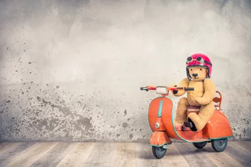 Acrylic prints Scooter Retro Teddy Bear toy in red helmet with goggles sitting on old children's pedal orange scooter from 60s front loft concrete wall background. Kid racer concept. Vintage style filtered photo