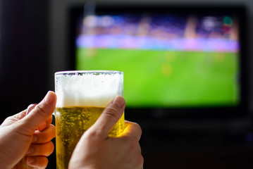 Glass cold beer on living room background with copy space. The woman's hand holds the mug beer. Selective focus, horizontal.