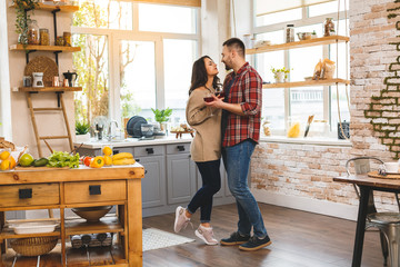 Dancing in kitchen. Young romantic couple celebrating engagement copy space. Cute young couple dancing at home, drinking wine.