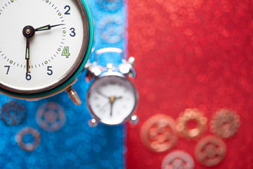 Alarm clock and small parts of watch on red and blue abstract background