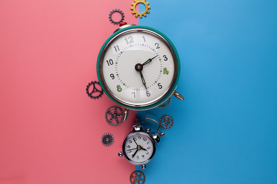 Two old alarm clocks and small gears, parts of the watch on a two-colored background