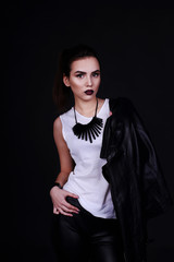  Fashion portrait of an attractive long hair young woman in a black leather jacket over a black background. Fine evening jewelry. Studio photography.