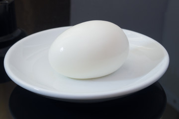 one boiled egg on white plate and black background