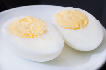 one boiled egg cut in half on a white plate and black background