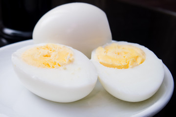 one boiled egg cut in half on a white plate and black background
