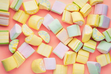 Top view randomly lying marshmallow in different colors on a pink background