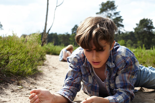 Boy lying on sandy path watching beetle
