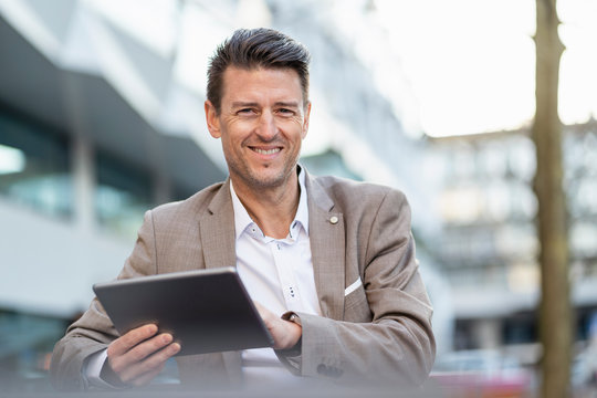 Portrait Of Smiling Businessman Using Tablet Outdoors