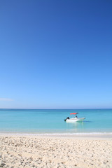 Boat Bobbing Off A Sunny Sandy tropical Beach in turquoise ocean with cloudless blue sky in the background.