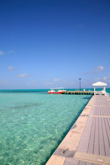 Obraz premium Vacation dream. view along a Caribbean Jetty towards a cabana and a couple of boats.