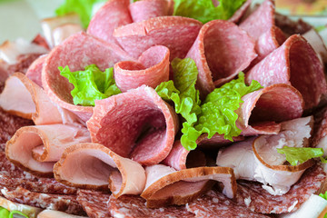 Sliced ham and raw smoked sausage rolls with lettuce leaves. Made dish.