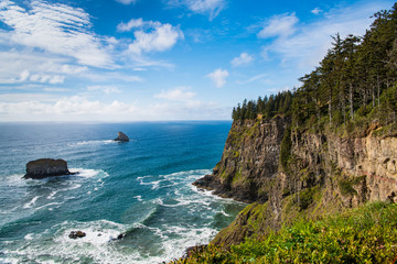 A coastline of high, green forested cliffs with a beautiful blue sea and sky - Cape Meares on the Oregon coast