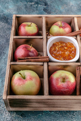 Close Up ripe apples, cinnamon, jam in a plywood box on a blue concrete background.