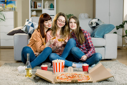 Special Event. Fast Food Delivery Service. Three Young Ladies In Casual Wear Eating Delicious Pizza, Popcorn And Drinking Wine At Their Fancy Party.