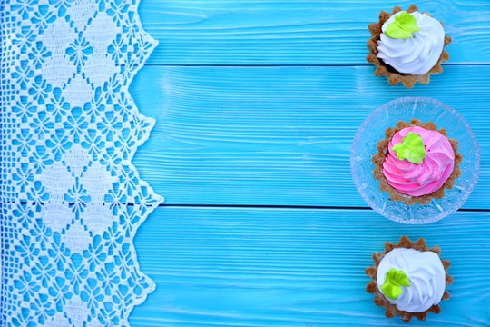 Three White And Pink Pastries On The Right, A Lace On The Left On A Blue Wooden Table, Top View