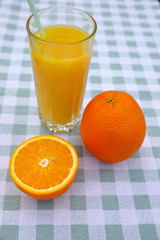 A glass of orange juice with a straw, oranges on a green-and-white checkered tablecloth, top view