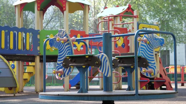 An empty carousel with wooden zebras is turning on the background of a bright multi-colored children's play complex.