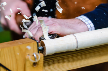 Shavings fly from the edge of a wood chisel as a man turns wood on a lathe.