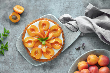 Top view of apricot tart with mint leaf on grey textured background