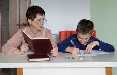 Grandmother helps her grandson to perform school homework.