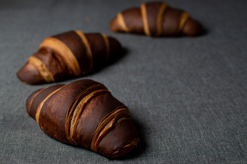 three chocolate brown croissants lying on a background, the background on the right is empty