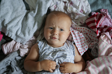 Funny Caucasian baby playing with bunch of clothes