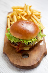 Hamburger with lettuce, cheese and bacon on a rustic wooden board on a white wooden background, side view. Close-up.