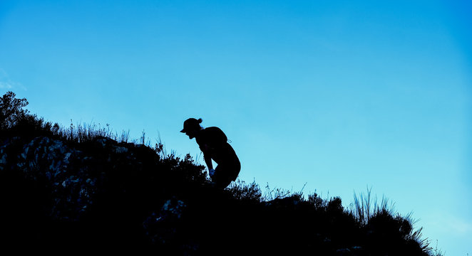 Dramatic silhouette of a person hiking and climbing a steep mountain