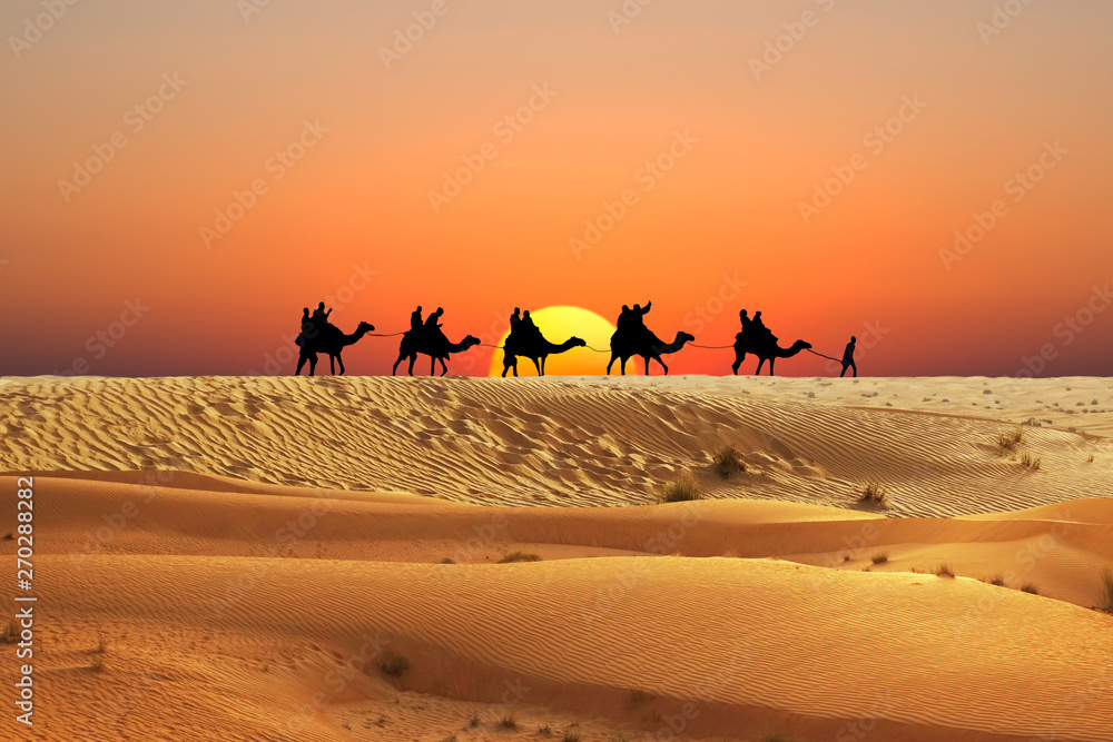 Wall mural Caravan of camels in Arabian Desert with people silhouettes at sunset